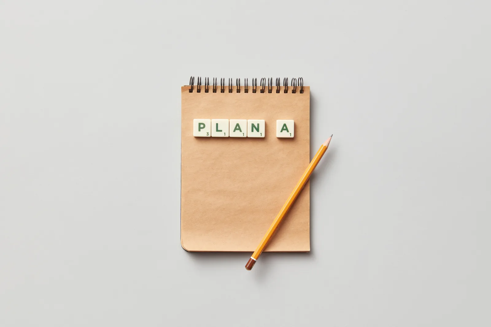 Top view of a notepad with a pencil and scrabble tiles spelling 'PLAN A' on a gray background. How to Build a Small Business Marketing Strategy
