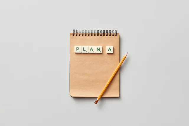 Top view of a notepad with a pencil and scrabble tiles spelling 'PLAN A' on a gray background. How to Build a Small Business Marketing Strategy